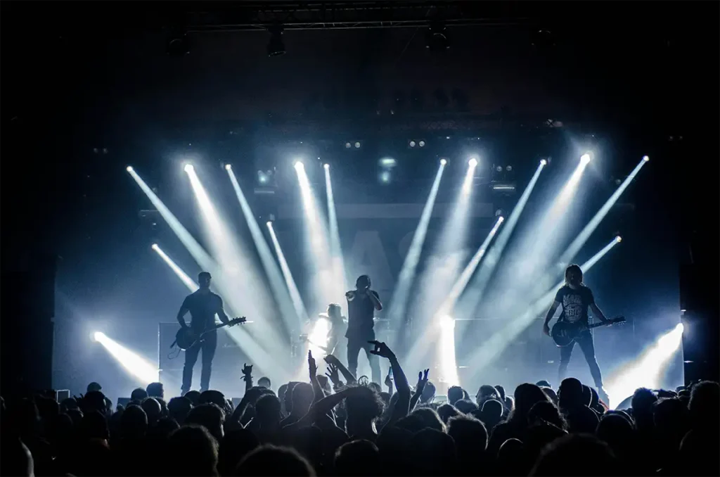A crowd of rock fans raising hands at a concert under vibrant stage lights.