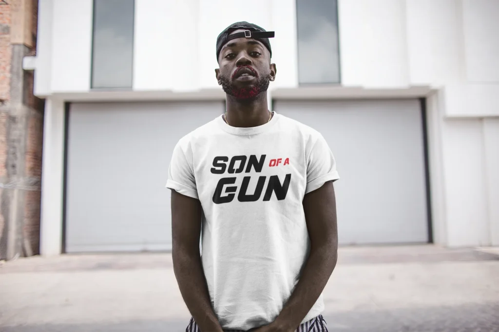 A young man wearing Trimnest t-shirt with sun of a gun text designed and printed on it, showcasing his individual style and cultural connection.